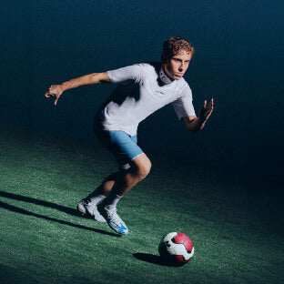 Jugador con chuteras Under Armour controlando un balón de fútbol en cancha